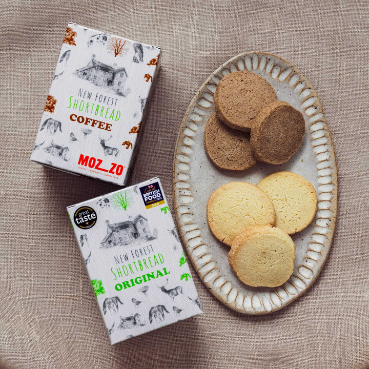 Two boxes of New Forest Shortbread with a plate of cookies on a textured surface