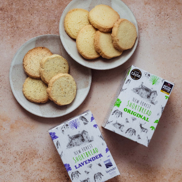 Two plates of shortbread cookies with two boxes of New Forest Shortbread on a textured surface.