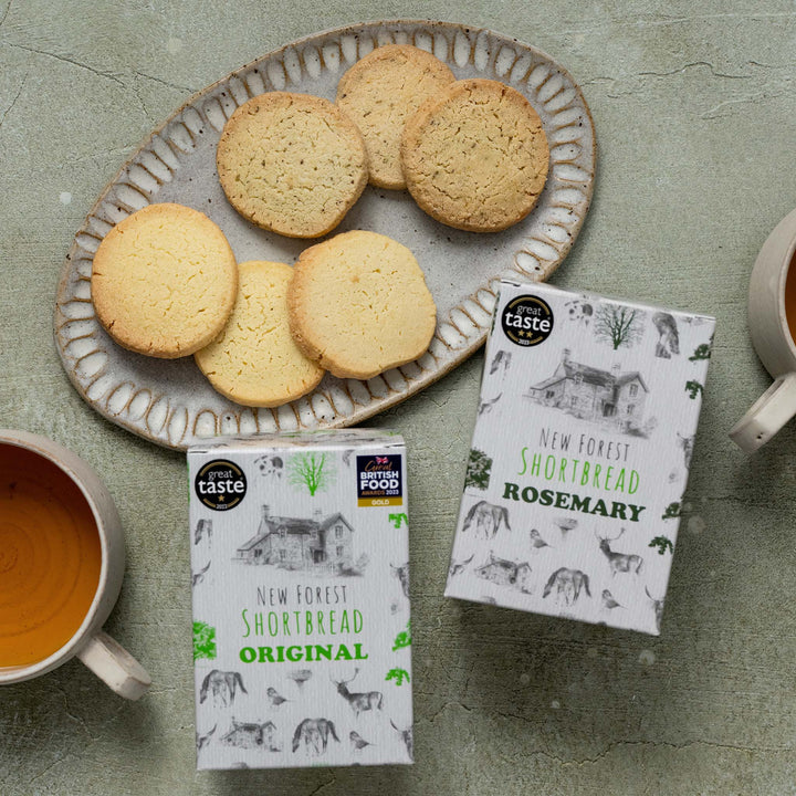 New Forest Shortbread cookies on a plate with packaging and a cup of tea on a textured surface.