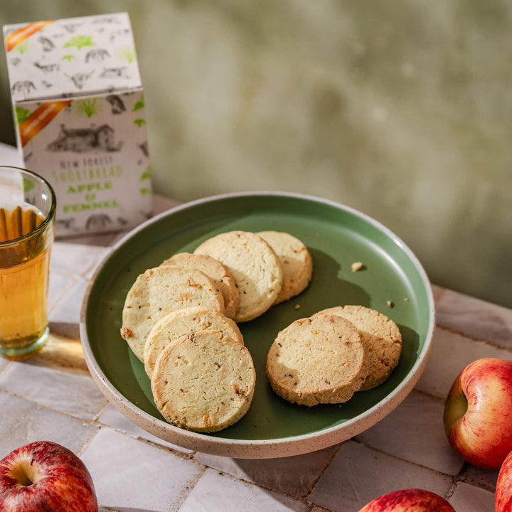Green plate with apple and fennel shortbread, a glass of tea, and apples on a table.