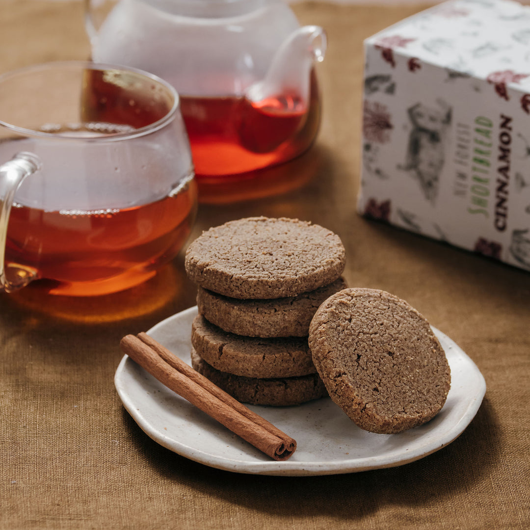 Shortbread cookeis on a plate with a cup of tea and cinnamon sticks on a wooden table.