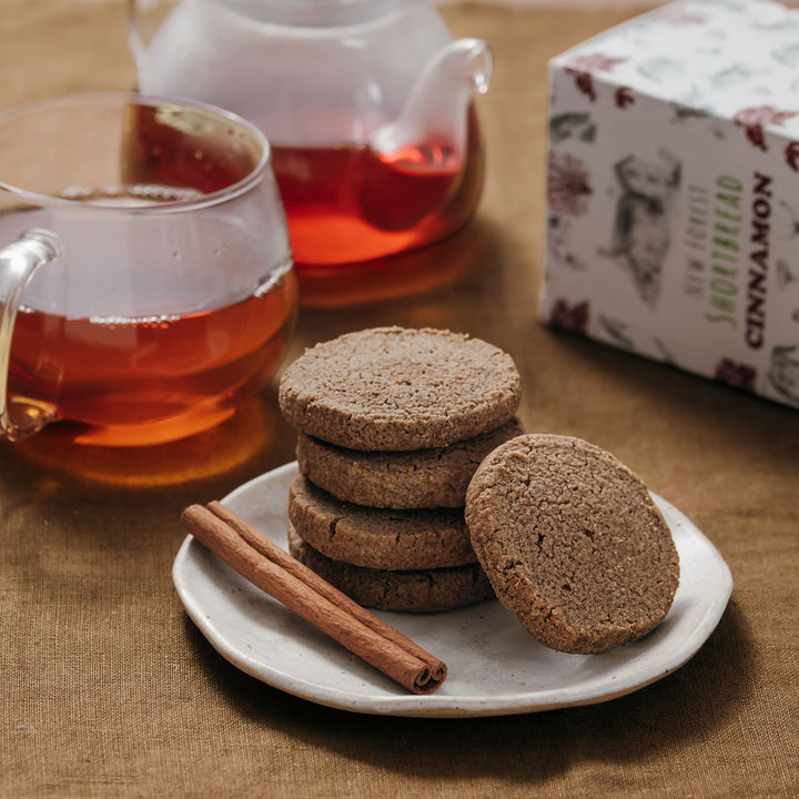 Shortbread cookeis on a plate with a cup of tea and cinnamon sticks on a wooden table.