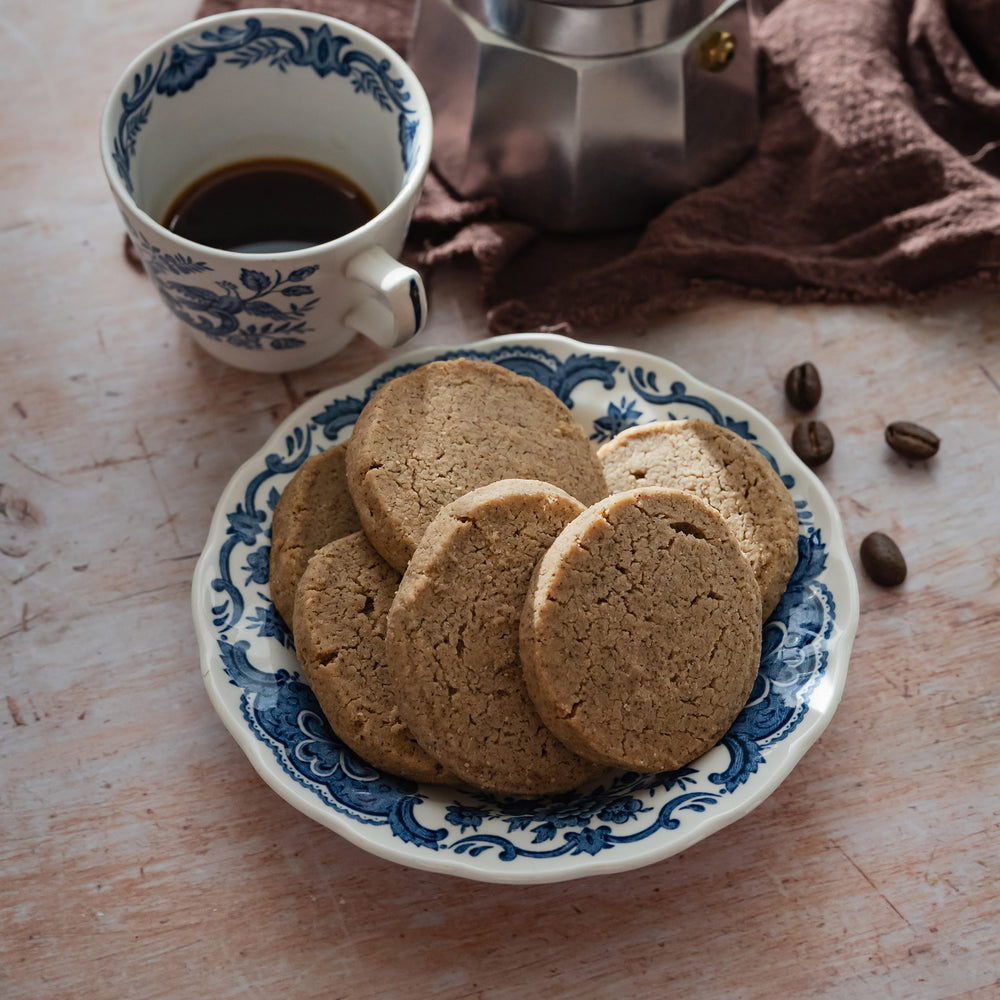 Coffee shortbread on a decorative plate with a cup of coffee and coffee beans on a wooden surface