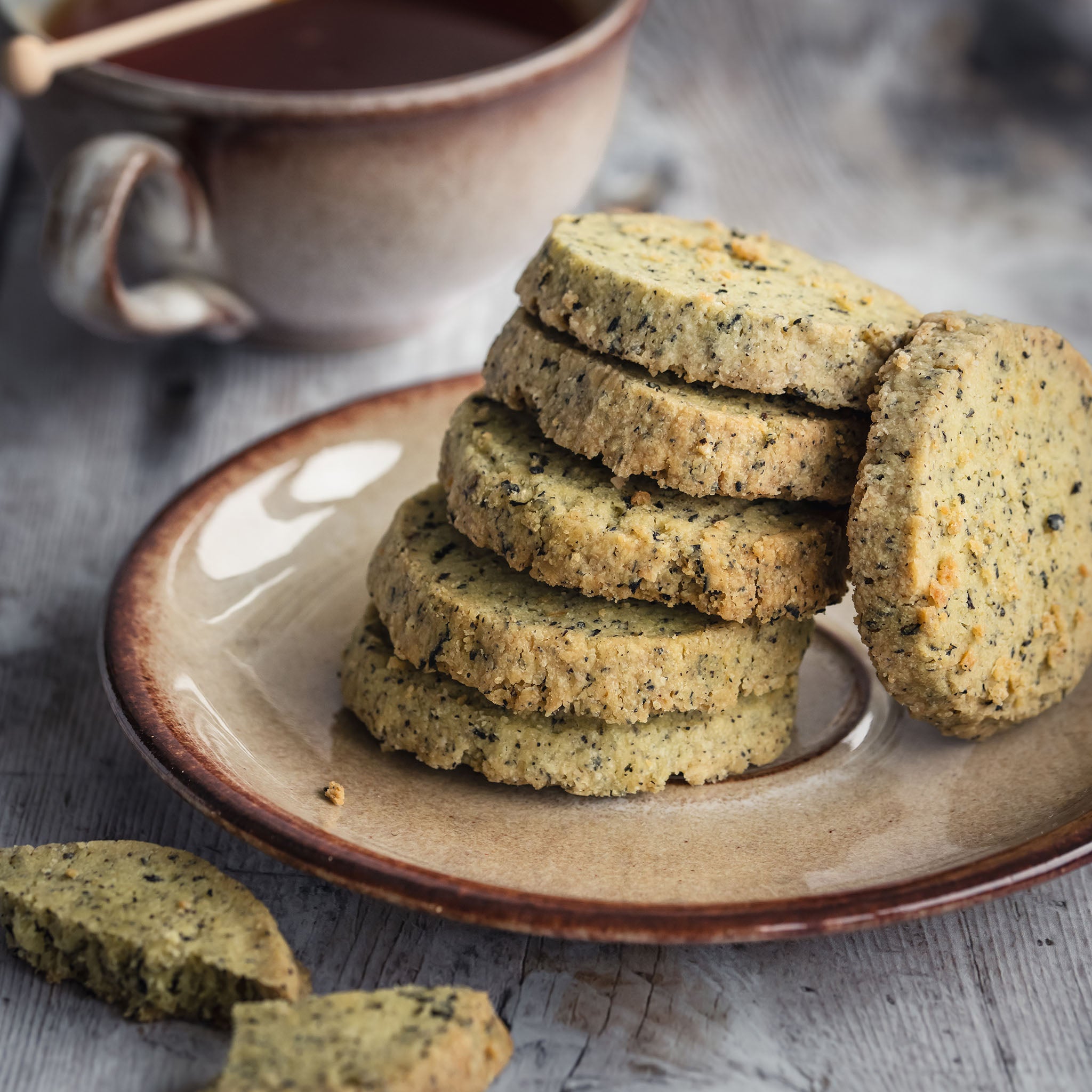 Stack of earl grey shortbread cookies on a ceramic plate with a cup of tea in the background