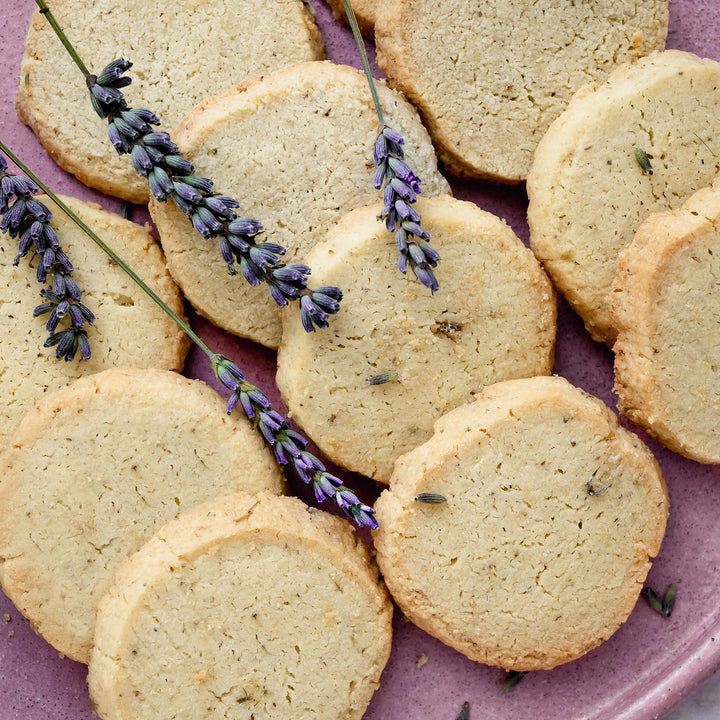 Shortbread with lavender flowers laid on rounds of lavender shortbread on a lilac coloured stoneware plate