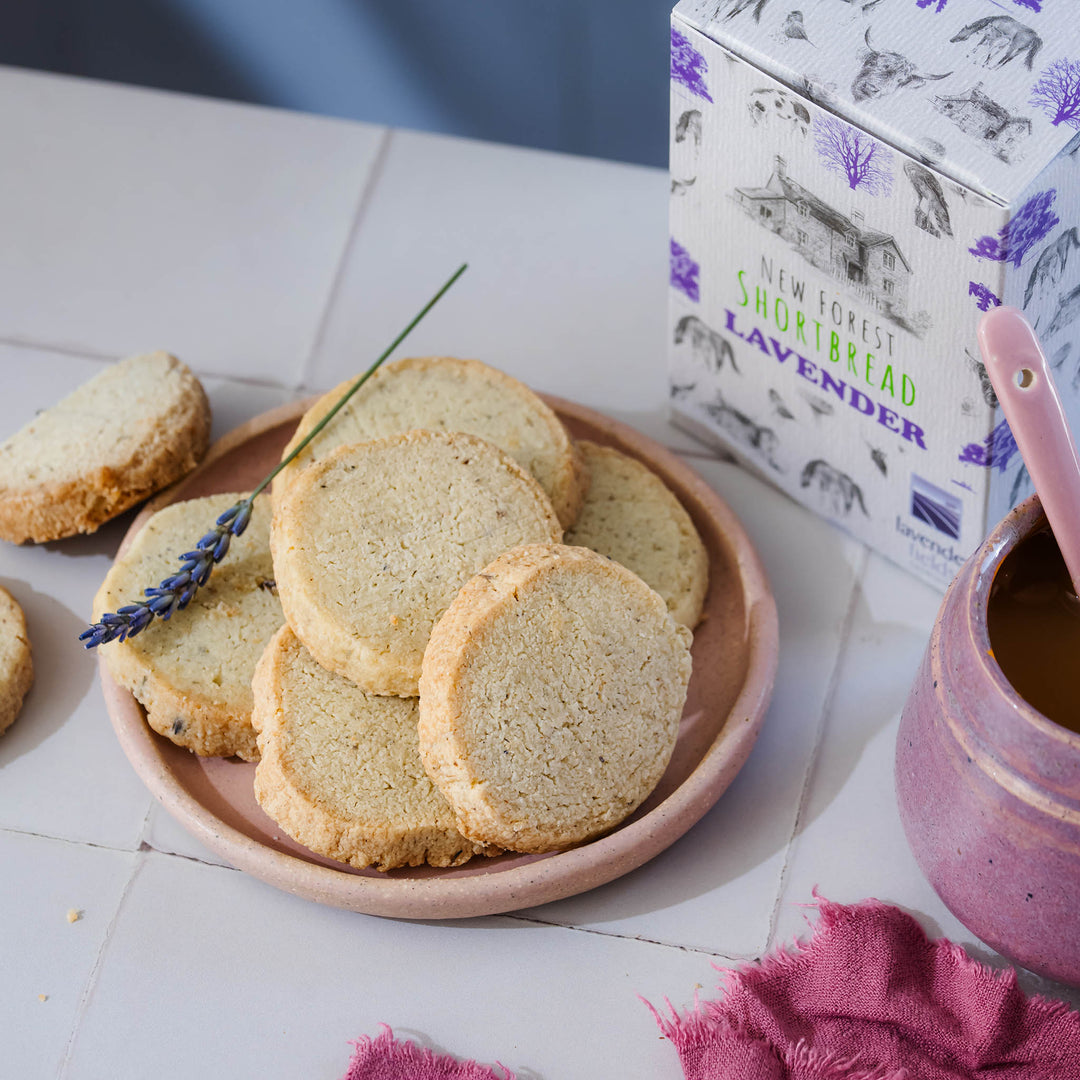 Rounds of lavender shortbread on a stoneware round tea plate with matching stoneware pestle and mortar bowl next to a box of lavender new forest shortbread