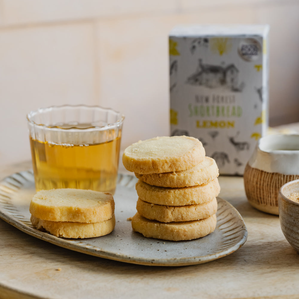 Stack of lemon shortbread biscuits on a plate with a glass of lemon tea and a box in the background.