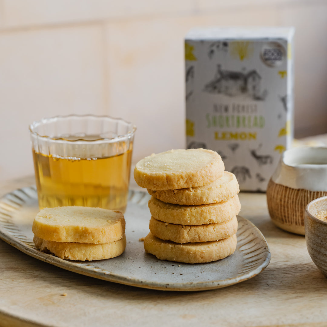 Stack of lemon shortbread biscuits on a plate with a glass of lemon tea and a box in the background.