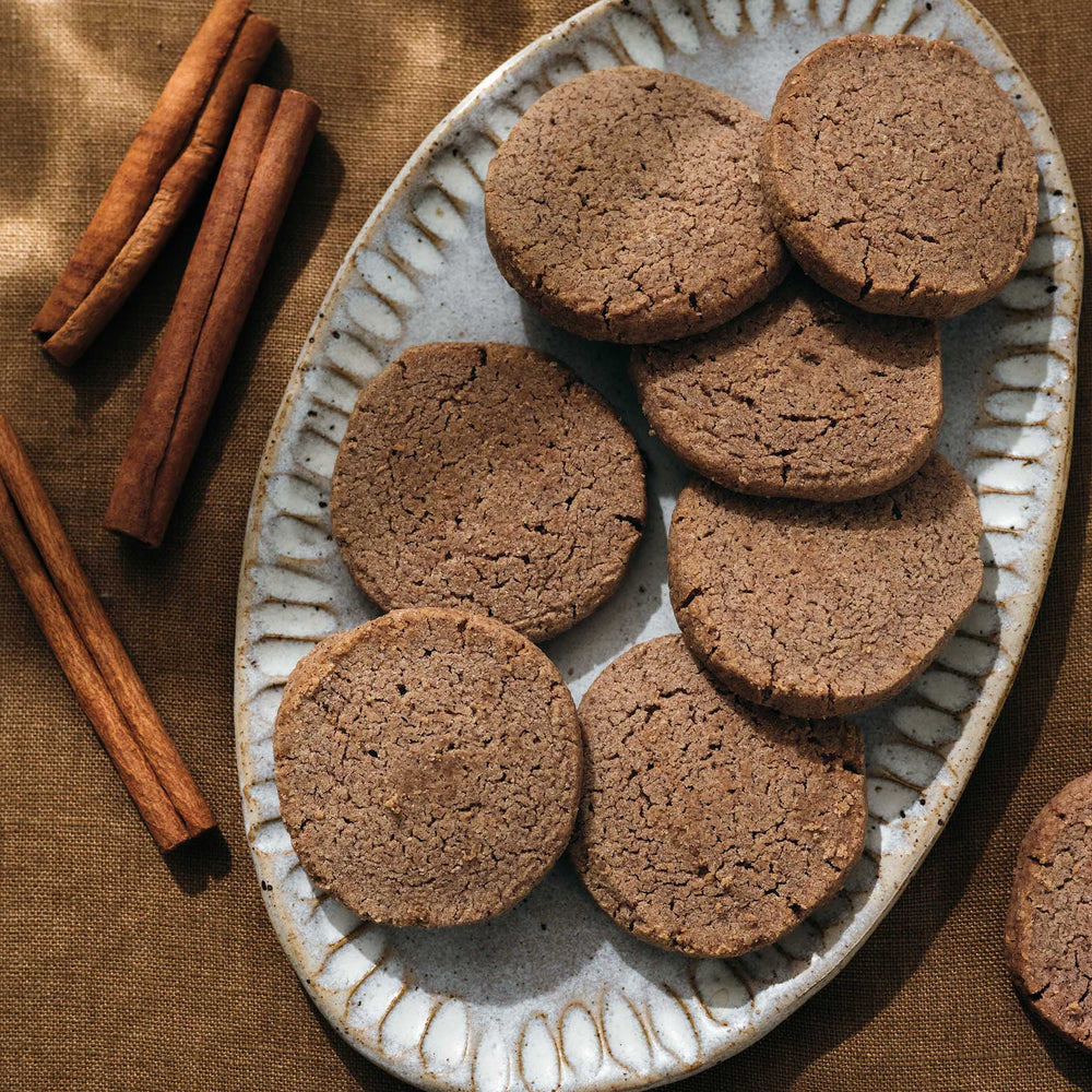 Cinnamon shortbread on a decorative plate with cinnamon sticks on a brown fabric background