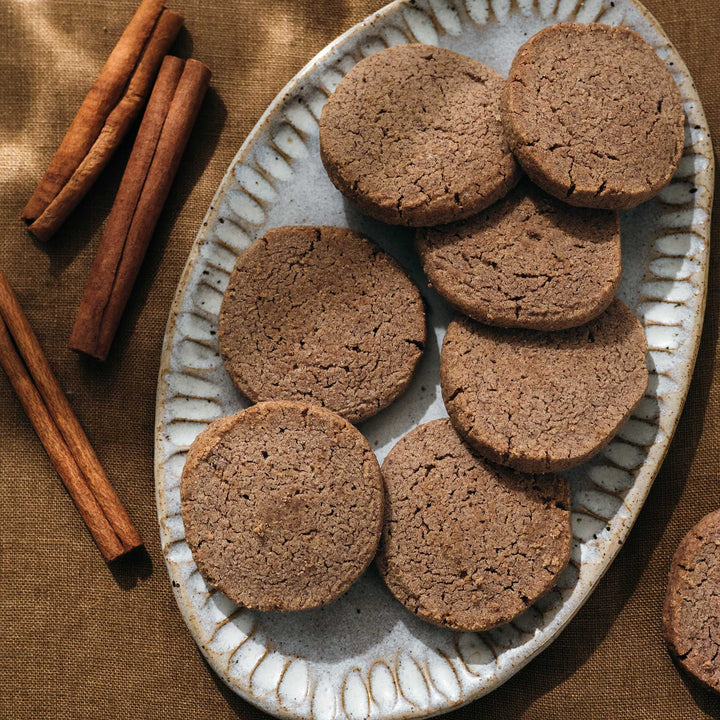 Cinnamon shortbread on a decorative plate with cinnamon sticks on a brown fabric background