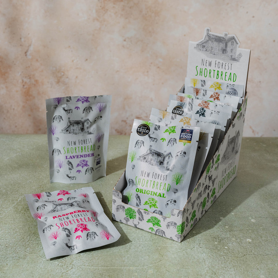 Display of New Forest Shortbread snack packs in an illustration of flora and fauna of the New Forest themed box, sitting on a textured surface with a neutral background