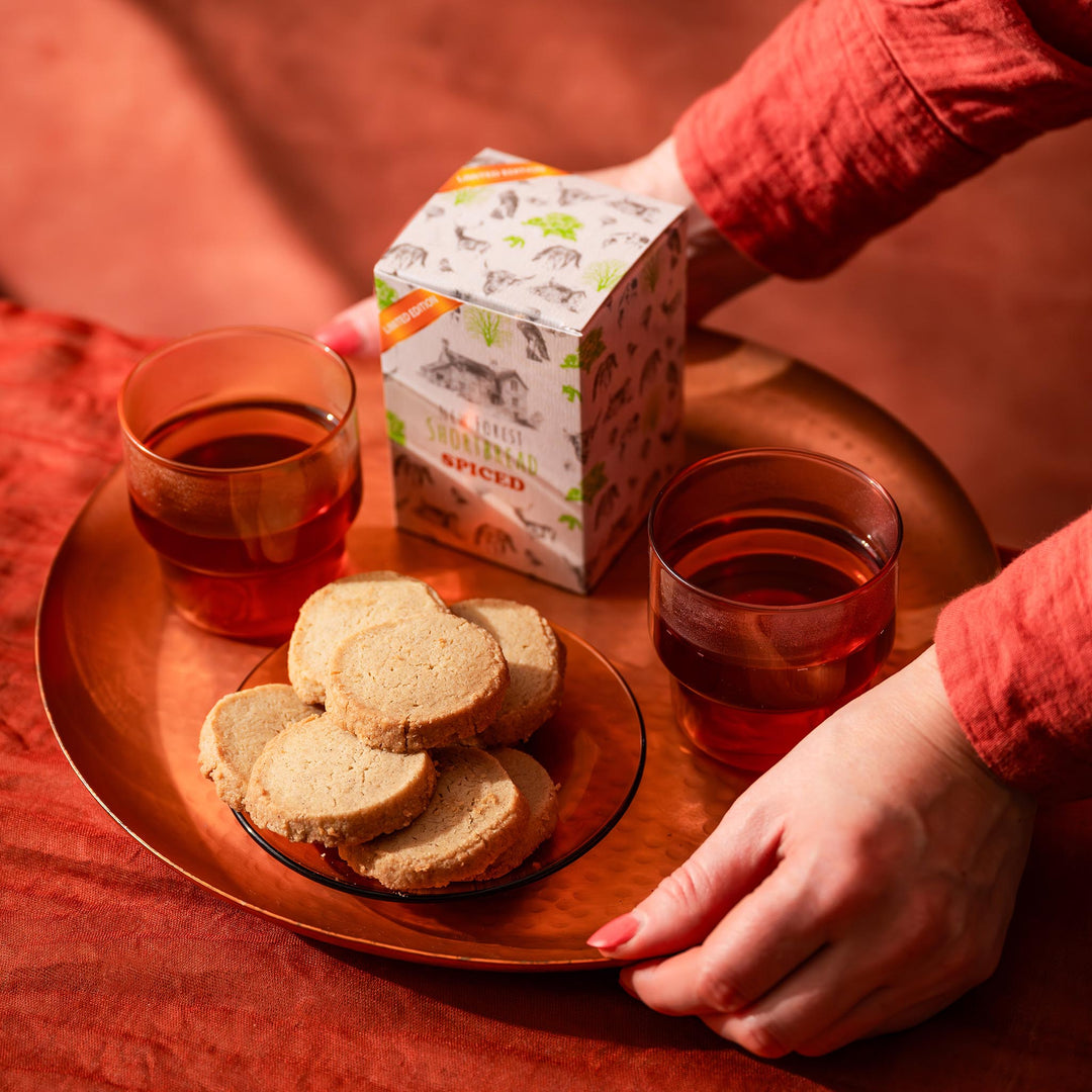 Spiced Flavoured Shortbread stacked on a plate with a box of biscuits and two cups of tea